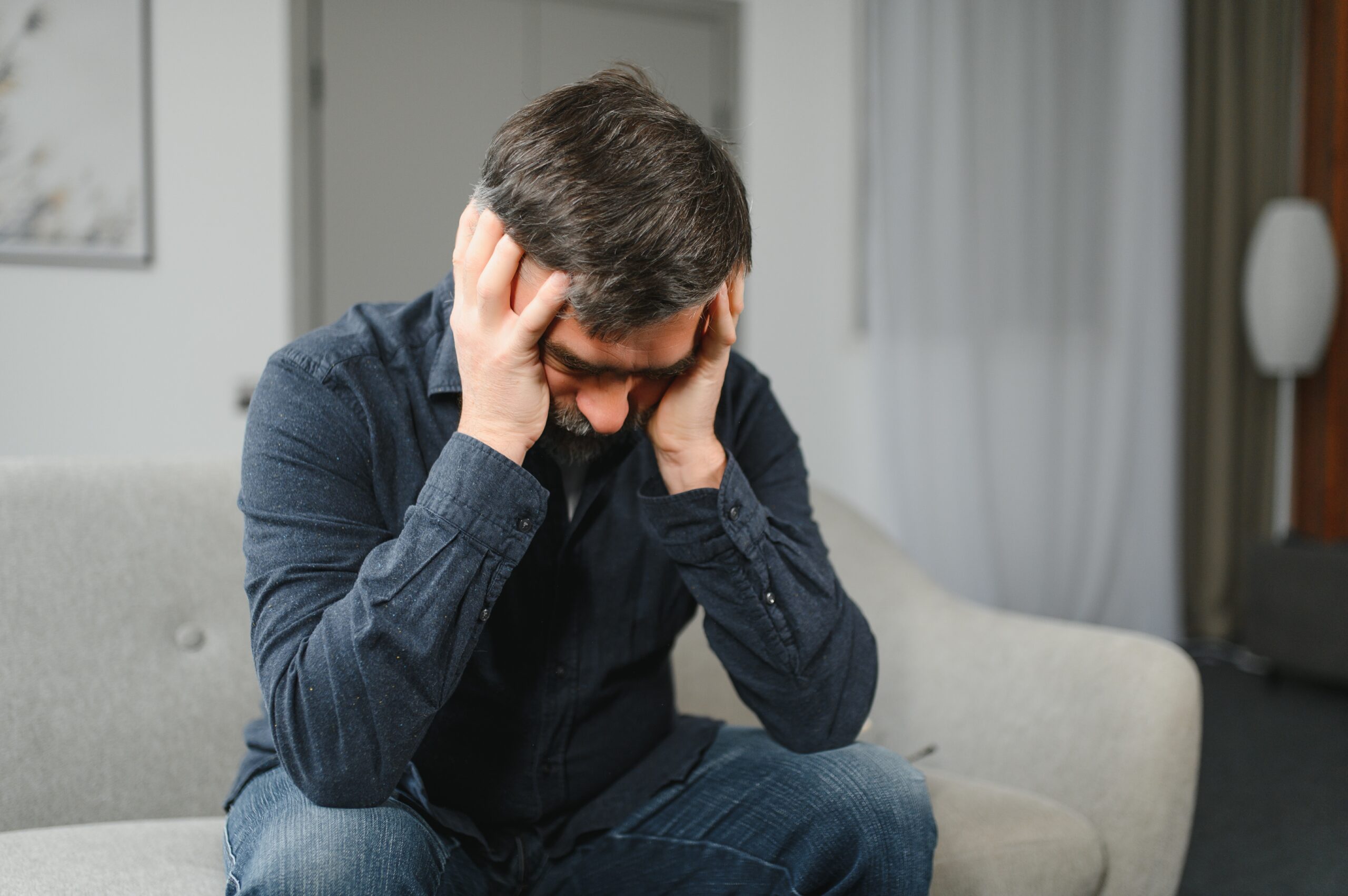 Closeup of middle-aged bearded man suffering from headache at home, touching his temples, panorama with copy space. Migraine, headache, stress, tension problem, hangover concept